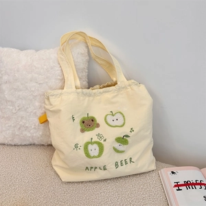 Detail of cute bear and apple embroidery on cream yellow canvas drawstring tote bag