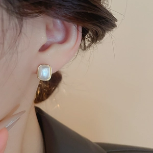 Gros plan de boucles d'oreilles perles carrées dorées portées avec un éclairage doux