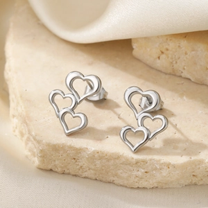 Three-heart hollowed stainless steel stud earrings in silver on stone and silk background