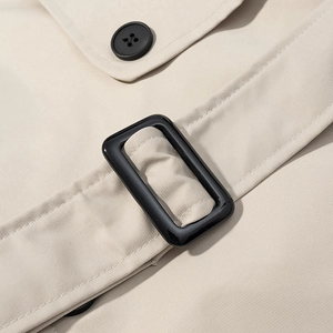 Détail du trench-coat beige montrant le tissu sergé et un bouton rond noir élégant