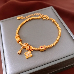 Detail of 24K gold-plated beaded bracelet with flower charm and red gemstone on velvet