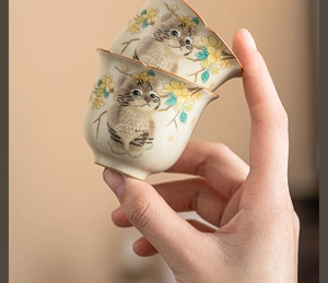 Detail of hand-painted cat and floral motifs on ceramic Ru kiln teacups held by hand