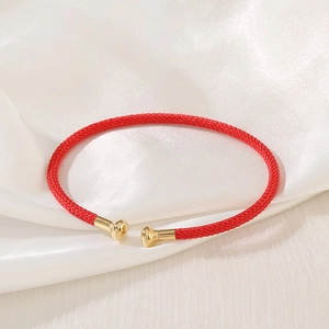 Detailed close-up of a red woven bracelet with gold metal end caps on white silk