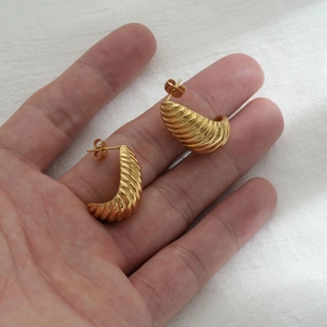 Close-up of golden croissant-style hoop earrings held in hand to show size and texture