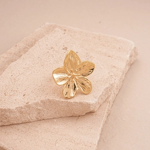 Detailed close-up of golden flower ring with hammer texture on natural rock base