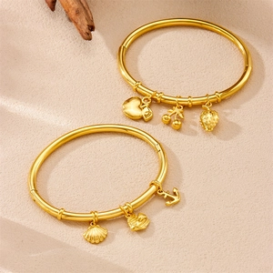 Gold stainless steel bamboo bracelets with ocean and fruit charms on warm sand background