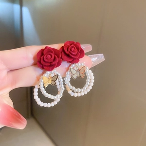 Dettaglio di orecchini a rosa in velluto rosso con perle e ciondolo a farfalla