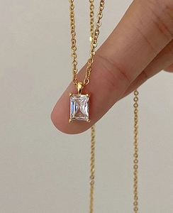 Close-up of gold chain necklace with emerald green rectangular zircon pendant in hand