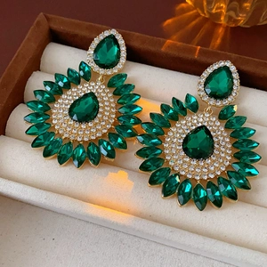 Macro shot of gold-plated drop earrings with marquise green crystals in a beige box