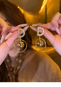 Close-up of gold dangle earrings with letter D zircon stones and hollow circular pendants