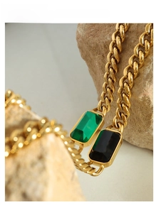 Close-up of gold Cuban chain necklace with green and black rectangular gemstones