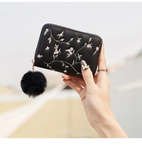 Detail of black PU leather short wallet featuring floral embroidery and a plush ball charm