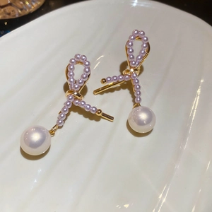 Dettaglio di orecchini a fiocco dorati con perle lavanda e pendente in perla bianca