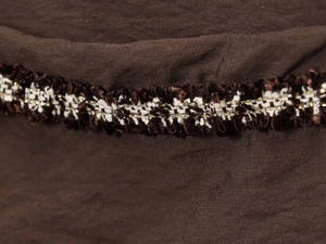 Detailed close-up of dark brown fabric texture and intricate woven trim on long sleeve shirt
