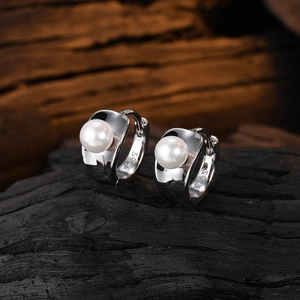 Macro view of S925 sterling silver pearl hoop earrings on dark wood background