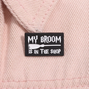 Vue rapprochée du pin's émaillé noir avec texte My Broom Is In The Shop sur velours rose