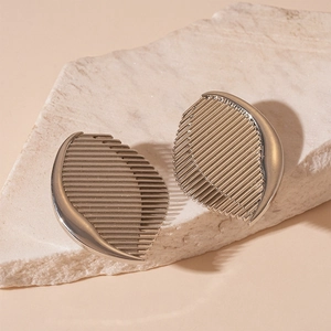Macro detail of silver half-moon earrings with vertical stripes on textured stone background
