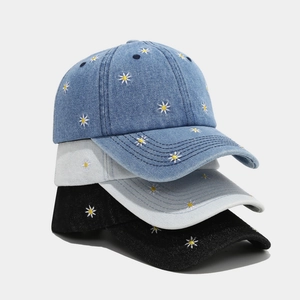 Détail de trois casquettes de baseball en jean avec motifs marguerites brodés