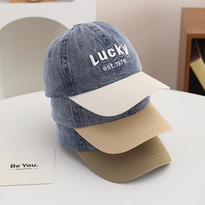 Detail of denim baseball caps with Lucky embroidery and colorful brims on white surface