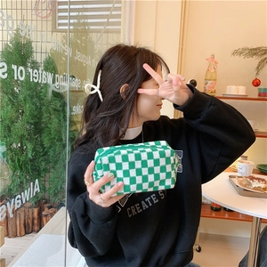 Green and white checkered knit pouch with zipper held by a hand in a cafe setting