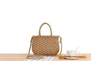 Detail of a beige woven straw bag with handle and shoulder strap on a wooden desk