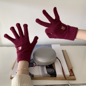 Close-up of wine red knitted glove with small bear embroidery on the ribbed cuff