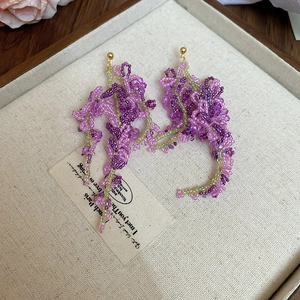 Detailed view of handmade purple and green bead flower fringe earrings on a beige tray