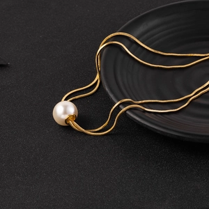 Macro shot of minimalist gold snake chain with a large round white pearl pendant