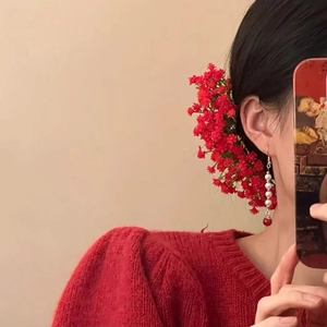 Spilla per capelli con fiori rossi e orecchini di perle con un maglione rosso a trecce