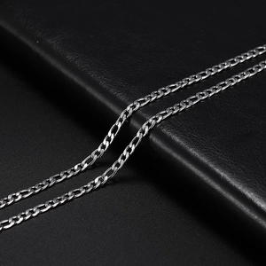 Close-up of silver stainless steel Figaro chain with polished links on black leather texture