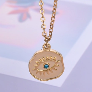 Close-up of 18k gold plated evil eye pendant with blue rhinestone and beige enamel