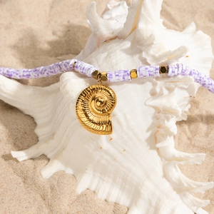 Détail du pendentif coquillage doré 18K avec perles violettes et blanches sur sable