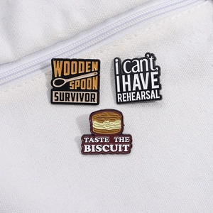 Three enamel pins with cookie and spoon designs pinned on a white canvas bag