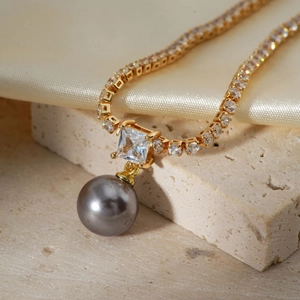 Elegant gold necklace featuring a square zircon and dark grey pearl on silk texture