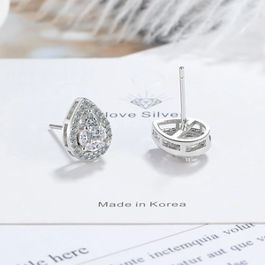 Macro view of silver water-drop zircon earrings on jewelry card with feather decor