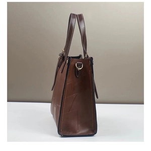 Detail view of deep brown leather patchwork tote bag with side metal buckles and stitching