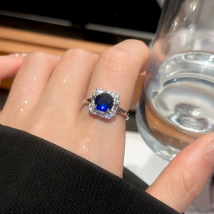 Close-up of deep blue cushion-cut gemstone ring with zircon halo on silver band
