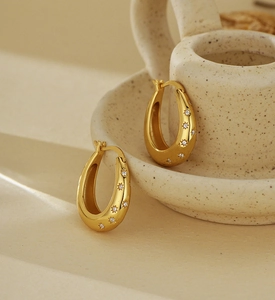 Macro detail of gold teardrop earrings with octagonal star diamond inlay on ceramic surface
