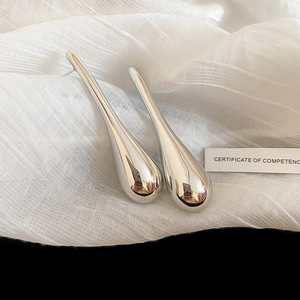 Close-up of silver teardrop earrings with a polished mirror finish on white silk