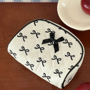 Detail of quilted cream makeup bag with black bow print and 3D satin bow on wood table