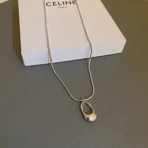 Silver stainless steel snake chain necklace with a hollow oval bean pendant on grey desk