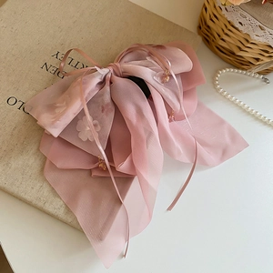 Dettaglio molletta per capelli in organza rosa con motivi floreali e ciondoli di perle