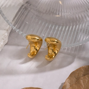 Detailed view of polished gold geometric arched earrings on elegant marble and glass surface