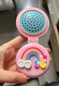 Detail of pink foldable hairbrush mirror showing a 3D rainbow design and blue bristles