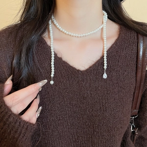 Detail of elegant pearl necklace with teardrop diamond pendant on brown V-neck sweater
