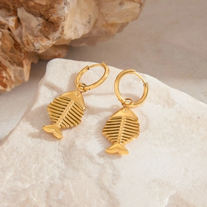 Macro detail of gold fishbone earrings with hoop closure on natural stone background