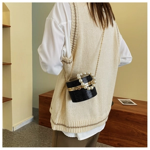 Elegant black cylindrical evening bag with pearl handle and gold chain on shoulder