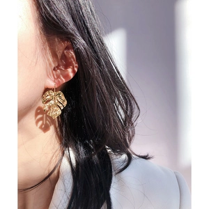 Exaggerated gold monstera leaf earrings with textured veins shown on a female model