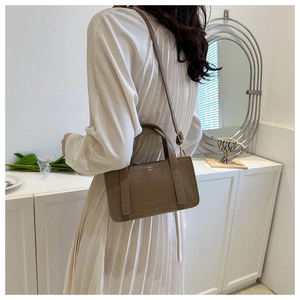 Side view of a khaki crocodile pattern square handbag with top handle and strap