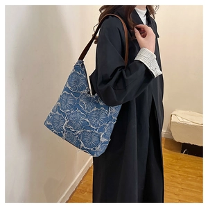 Close-up of blue denim tote bag featuring white frayed floral patterns and brown strap